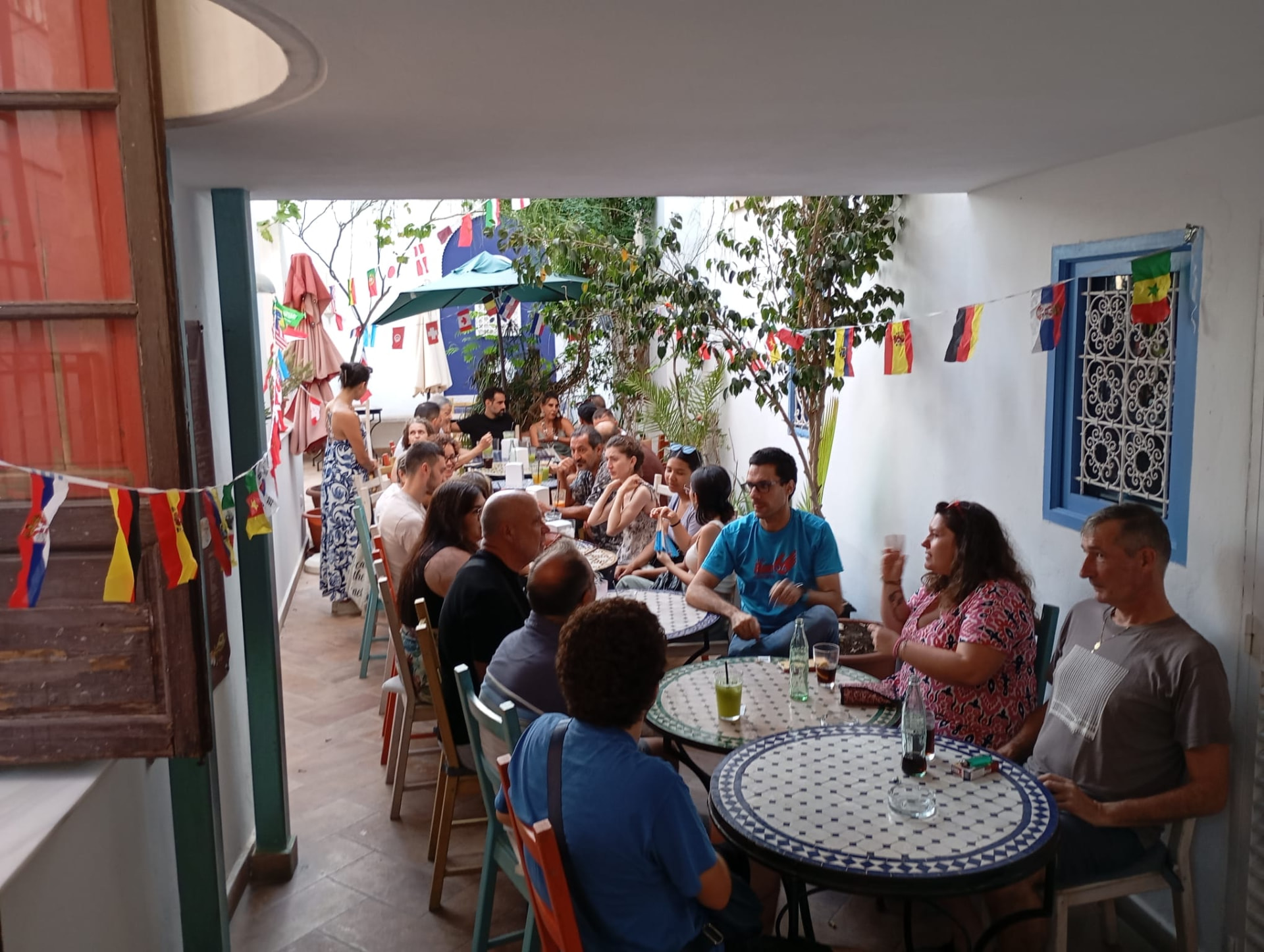 Language-exchange guests around mosaic tables in a whitewashed courtyard