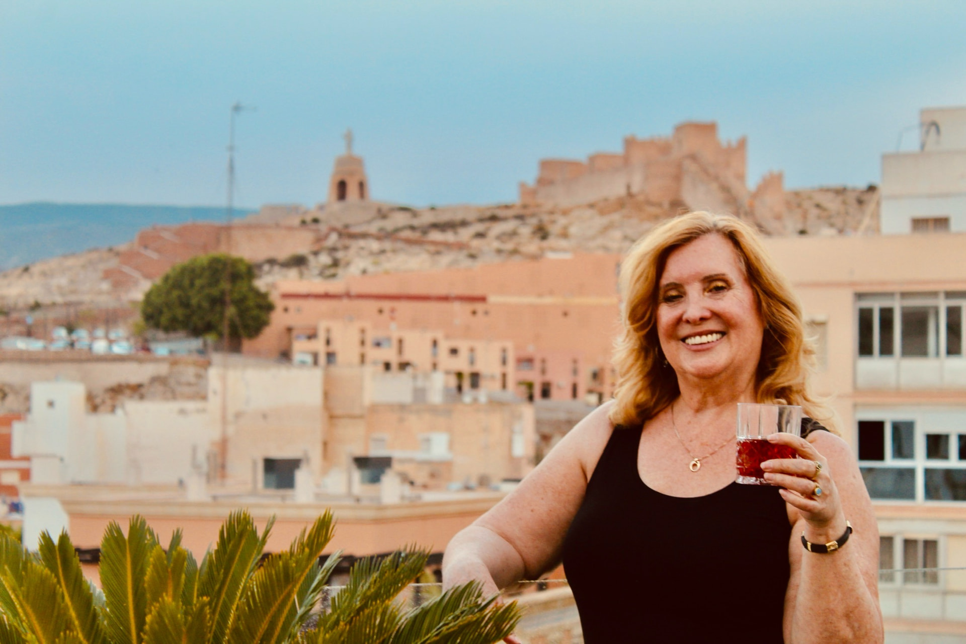 Magnette welcoming guests with a drink on a rooftop terrace beneath the Alcazaba